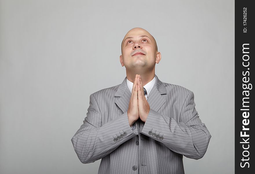 Bald businessman in a gray suit with a gray background makes various hand gestures