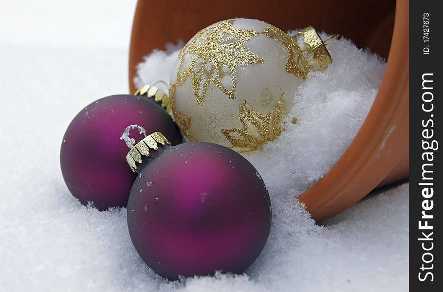 Christmas ornaments in a clay pot that is toppled over in the snowy garden. Christmas ornaments in a clay pot that is toppled over in the snowy garden.