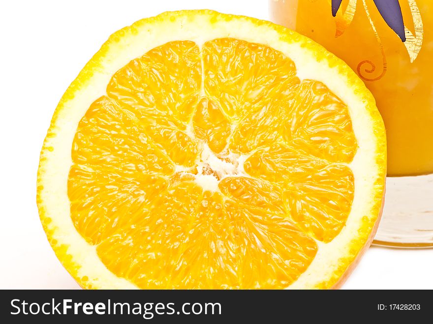 One big orange near a small glass with juice