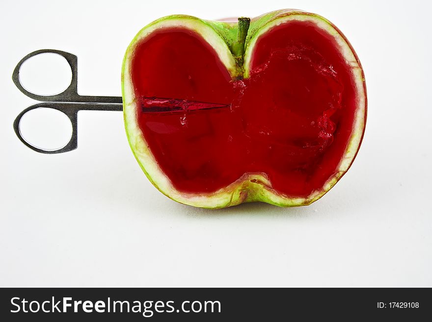 Scissors penetrate half apple filled with red jelly. Scissors penetrate half apple filled with red jelly
