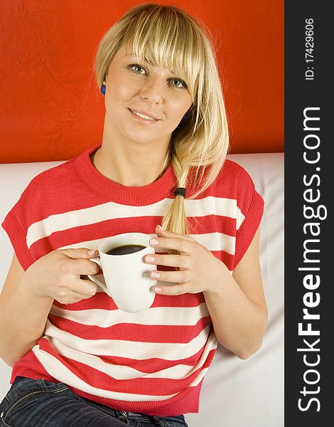 Beautiful young woman is drinking coffee from a white mug sitting on the couch. Beautiful young woman is drinking coffee from a white mug sitting on the couch