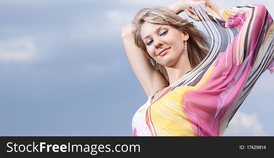 Outdoor portrait of a young lady on a blue cloudy sky background. Outdoor portrait of a young lady on a blue cloudy sky background