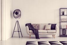 Black Lamp Next To Beige Sofa With Blanket And Pillows And Shelf With Books, Copy Space On Empty White Wall Stock Photos