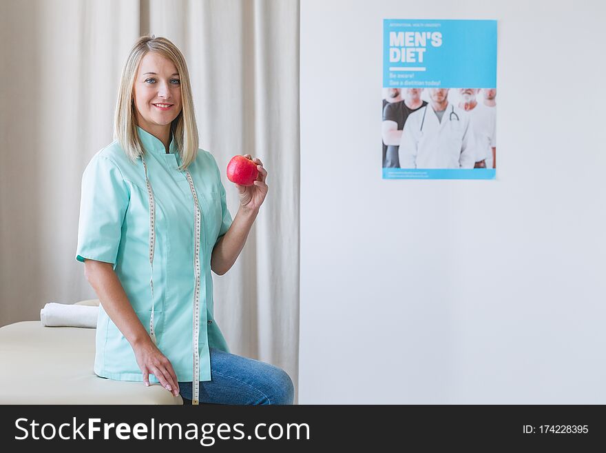 Beautiful Dietitian Is Standing In The Office Holding An Apple