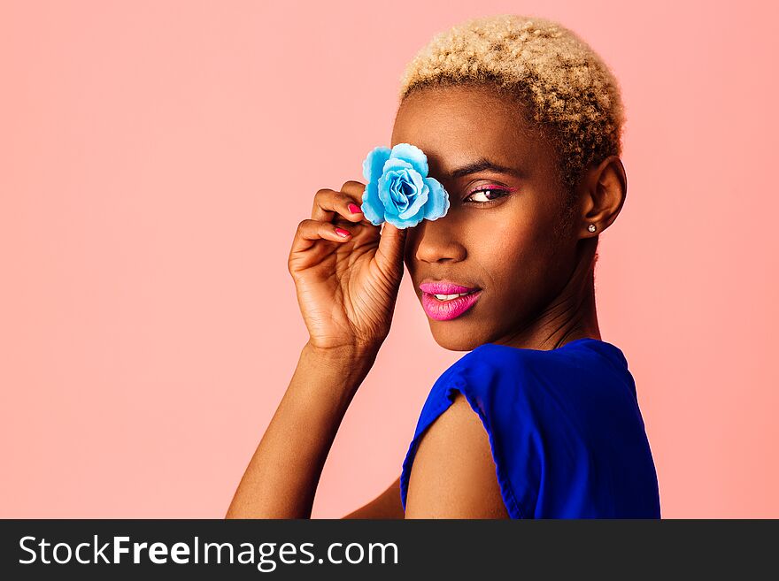 Portrait of  a beautiful young woman covering eye with blue rose flower, with trendy fresh makeup of pink lips and eyeliner