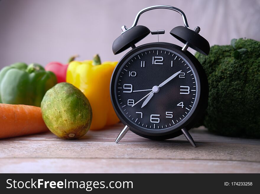 Close up of alarm clock and vegetable on table.