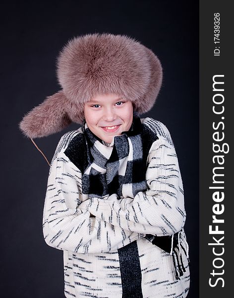 Portrait of a cheerful boy in winter hat on a dark studio background