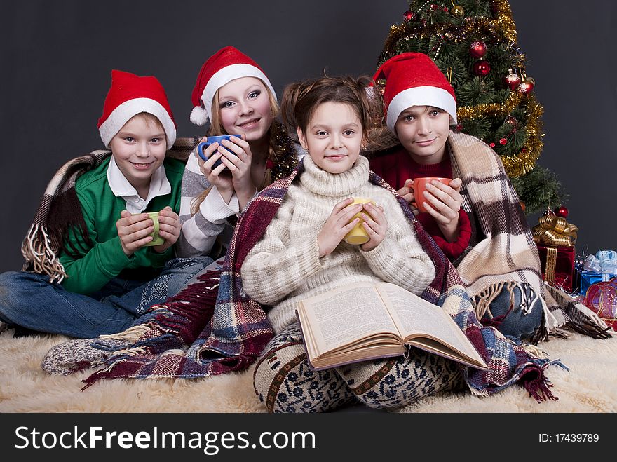 Four children near a decorated Christmas tree waiting for Santa Claus