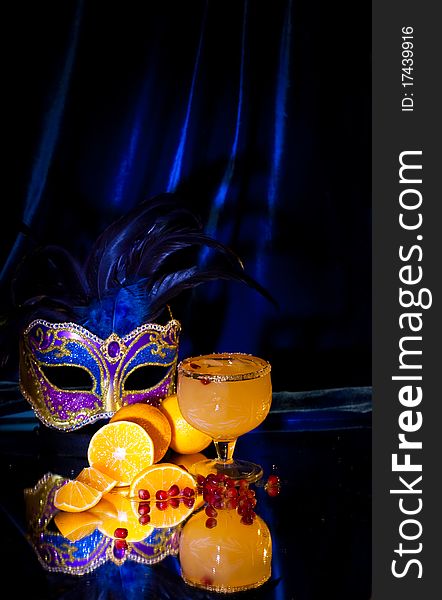 Drink in a glass, tangerines, grains of a pomegranate and a mask on a dark blue background. Drink in a glass, tangerines, grains of a pomegranate and a mask on a dark blue background