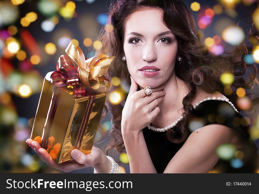 A cute young girl holding a christmas gift,dark background with christmas light bokeh. A cute young girl holding a christmas gift,dark background with christmas light bokeh