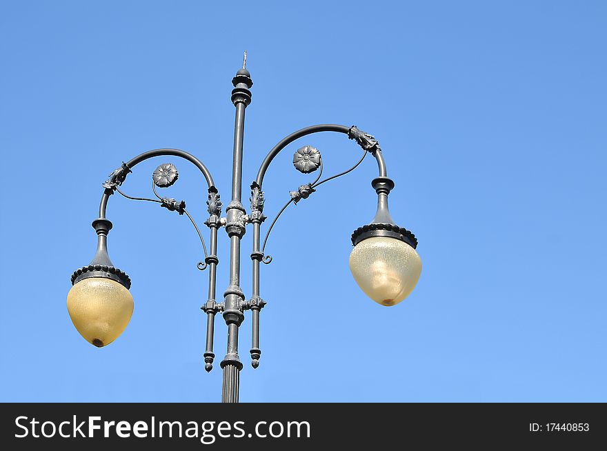 A photo of an old street lamppost against a blue sky. A photo of an old street lamppost against a blue sky.