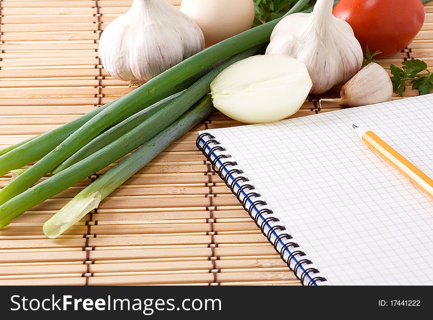 Notebook with pencil, garlic, tomato and onion on straw texture. Notebook with pencil, garlic, tomato and onion on straw texture