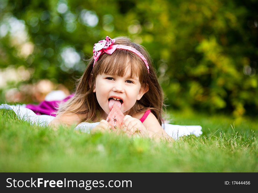 Smiling girl on the meadow eating watermelon