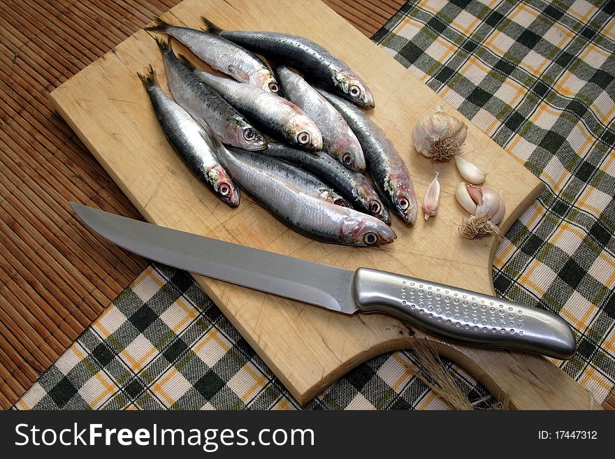 Fresh sardine on cutting board with knife and garlic by side. Fresh sardine on cutting board with knife and garlic by side