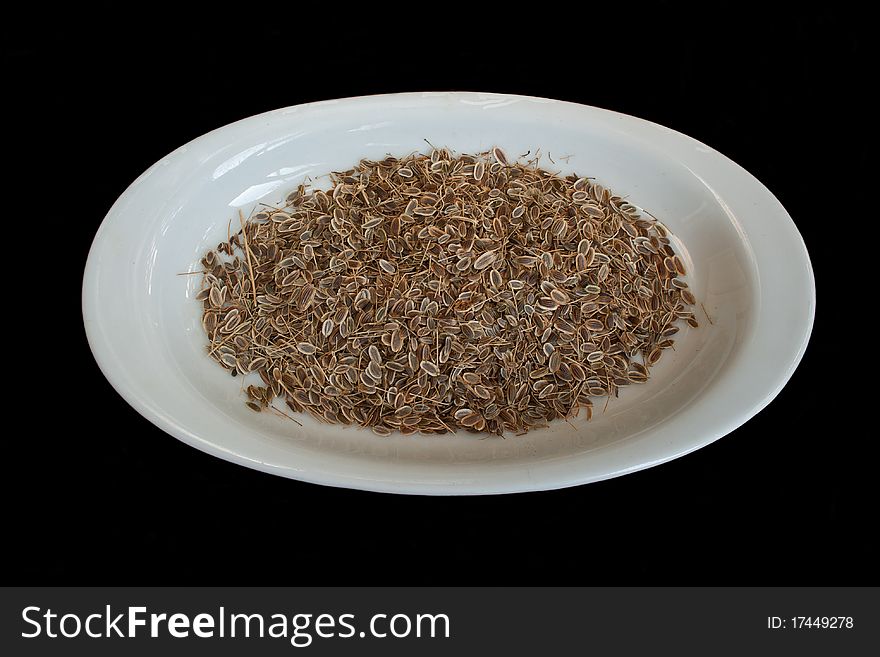 Dry dill seed on white oval plate in isolated on black