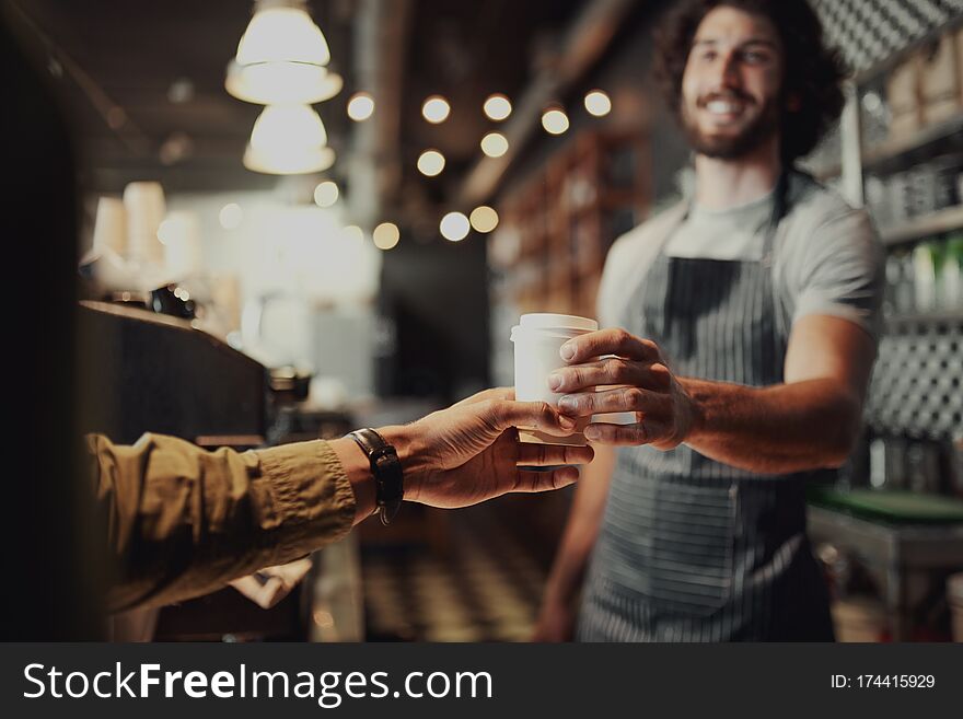 Young men waiter standing in cafe gives the coffee to men client. Young men waiter standing in cafe gives the coffee to men client