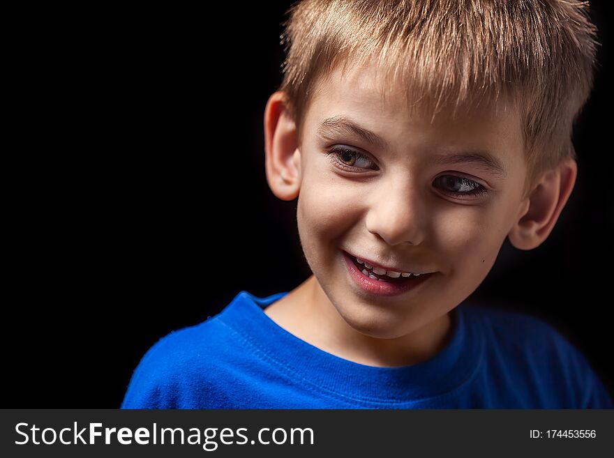 Portrait the face of the boy `s smiling child close-up against a black background. Emotions. Portrait the face of the boy `s smiling child close-up against a black background. Emotions