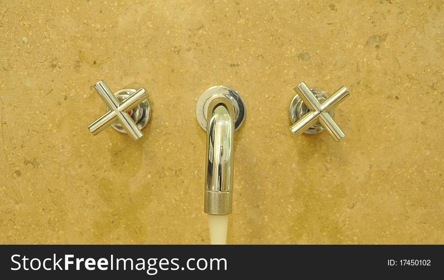 Metallic Faucet on yellow Ceramic wall with water drop