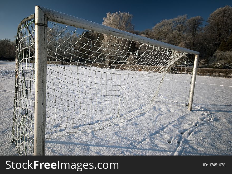 Soccer goal with icy net and soccer field outdoors in winter snow all over. Soccer goal with icy net and soccer field outdoors in winter snow all over.