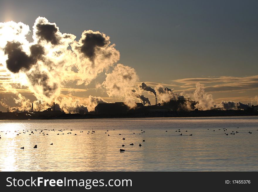 Sunrise through steam clouds along industrial shoreline