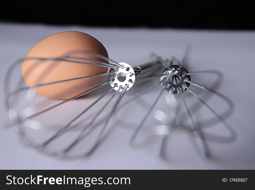 Macro closeup of a metal egg whisk with a single egg inside. Narrow dof. Macro closeup of a metal egg whisk with a single egg inside. Narrow dof