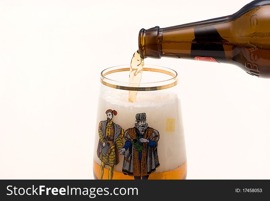 Light foamy beer is poured out of the bottle in glass on a white background