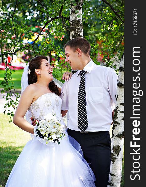 Joyful bride and groom near birches on grass in park