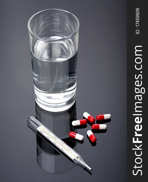 Pills, thermometer and glass of water over dark background