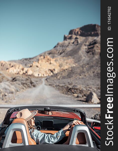 Young woman traveling by convertible car on the picturesquare road on the desert valley, rear view. Carefree lifestyle and travel concept. Young woman traveling by convertible car on the picturesquare road on the desert valley, rear view. Carefree lifestyle and travel concept