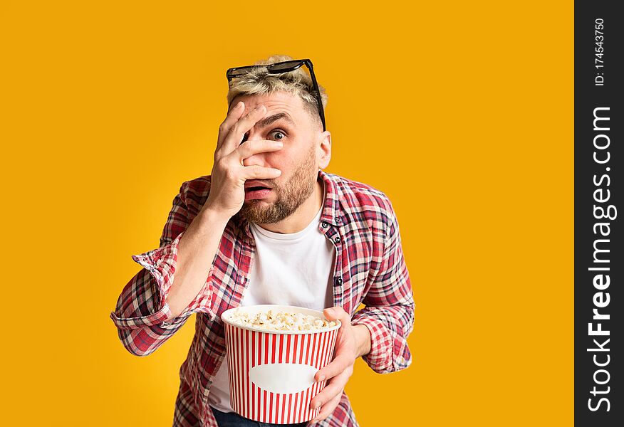 Scary movie. Shocked guy closes eyes his hand, holding bucket of popcorn, empty space