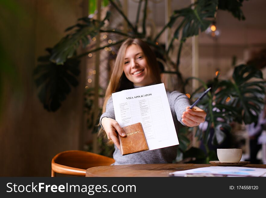 Focus on visa aplication, pen and passport in young woman hands at travel agency cabinet. Concept of execution of document for emigration. Focus on visa aplication, pen and passport in young woman hands at travel agency cabinet. Concept of execution of document for emigration.