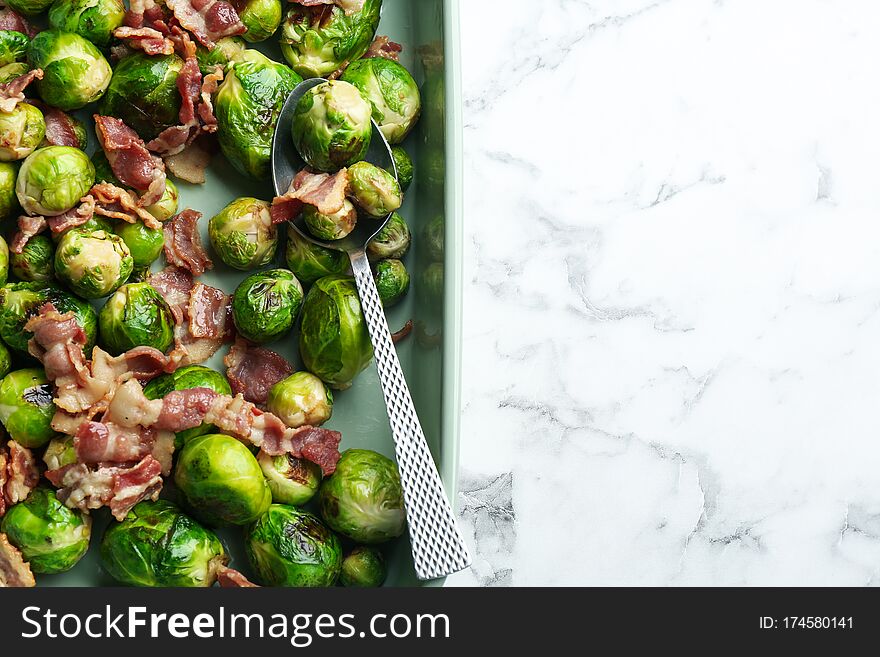 Delicious Brussels sprouts with bacon on white marble table, top view. Space for text