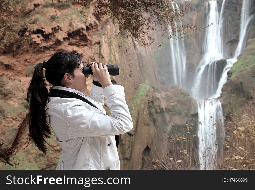 Young woman observing Ouzoud waterfalls with binoculars. Young woman observing Ouzoud waterfalls with binoculars