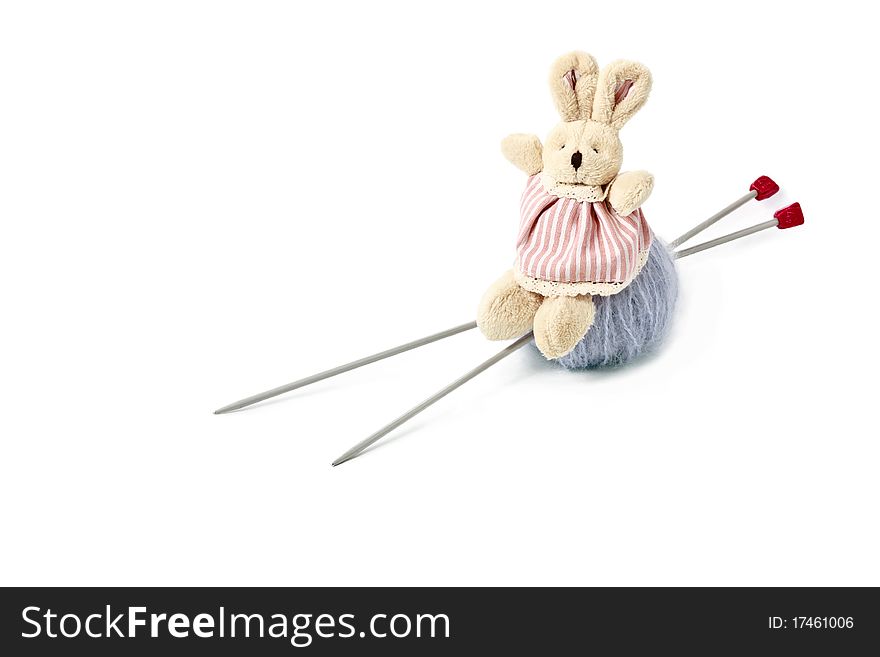 Toy little doe rabbit sitting on grey woolen mohair clew with knitting needles isolated on white background. Toy little doe rabbit sitting on grey woolen mohair clew with knitting needles isolated on white background