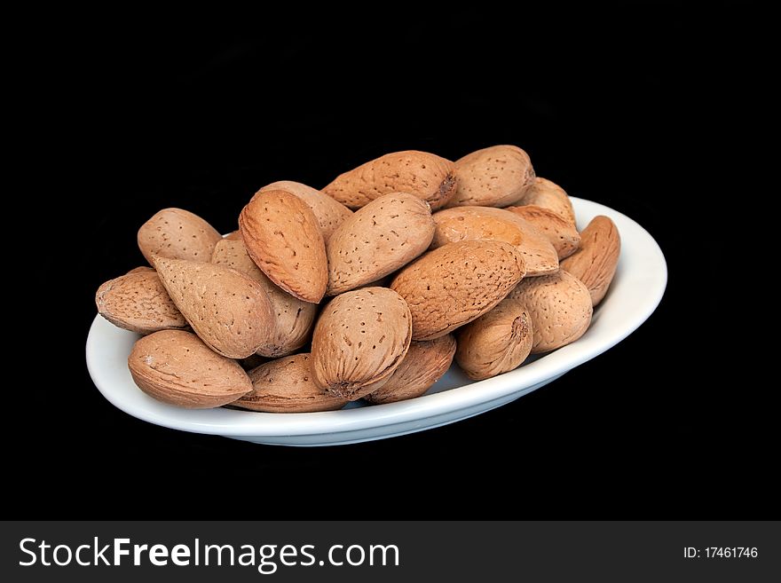 Almonds in nutshell on small oval plate in isolated over black