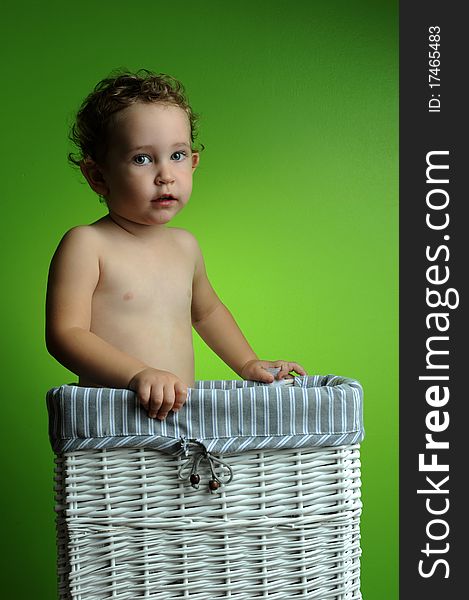 Baby sitting in a basket over a green background wall