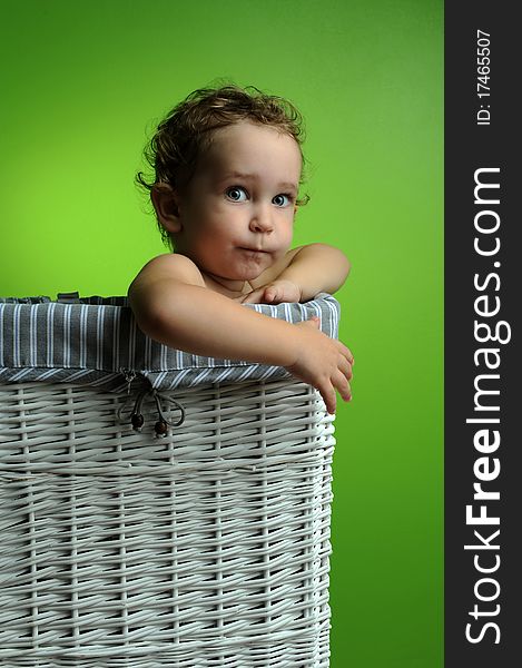 Baby sitting in a basket over a green background wall