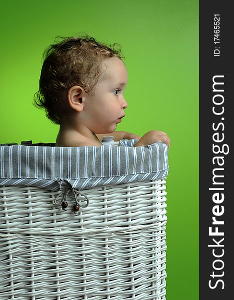 Baby sitting in a basket over a green background wall