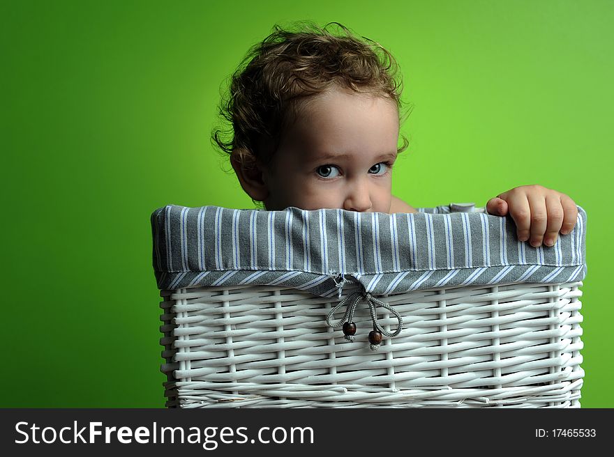 Baby sitting in a basket over a green background wall