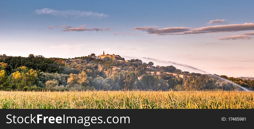 Watering a field of maize with Italian hill top village in background in early morning. Watering a field of maize with Italian hill top village in background in early morning