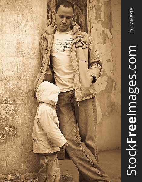 Man leaning against the column of a shabby building, child on the foreground. Man leaning against the column of a shabby building, child on the foreground