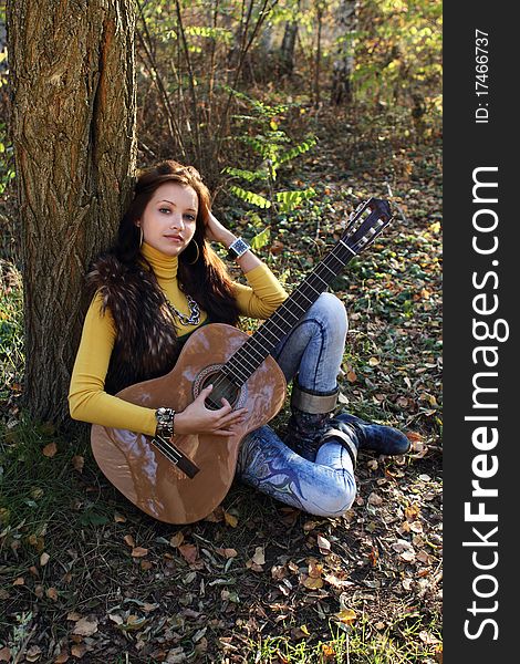 Beautiful brunette guitar player girl in the autumn forest