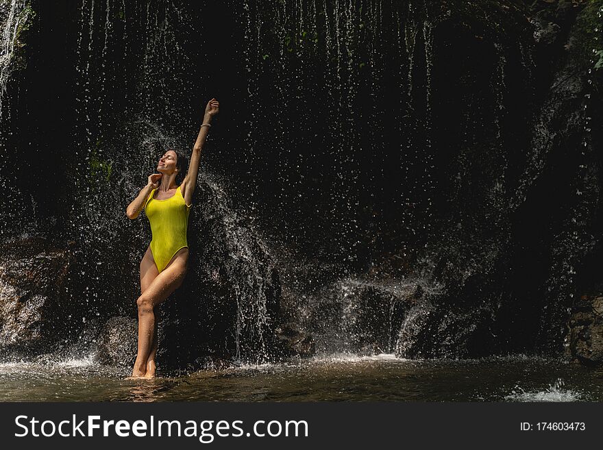 Kind young woman wearing swimsuit while having stop near waterfall during excursion. Kind young woman wearing swimsuit while having stop near waterfall during excursion