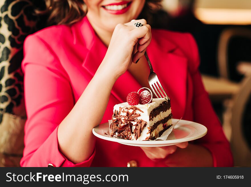 Close up image of woman eating cake Black Forest decorated with white chocolate and raspeberries