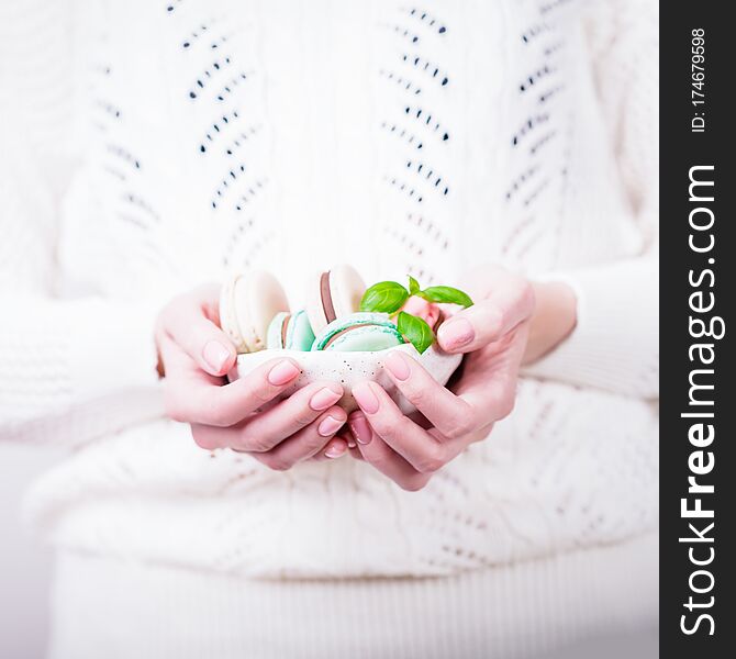 Beautiful female hands holding bowl of french colorful macaroons or macarons on light background