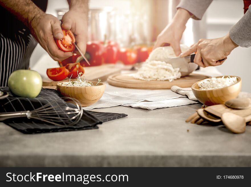 Women`s And Man`s Hands Preparing Meals. Preparation Of Dishes On A Wooden Kitchen Table In The Sunlight.