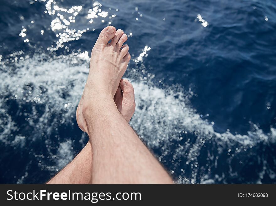 Bare feet hang down over azure water, splashes, sun patches of light on water,  sailing, sunny weather, sun reflections, summer, vacation