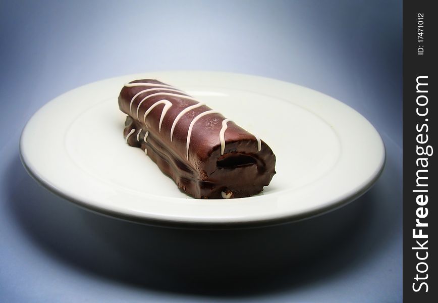 One small chocolate roll cake on plate. Dark blue background