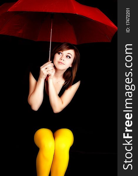 A woman holding a red umbrella and wearing yellow tights peeking out into the darkness. A woman holding a red umbrella and wearing yellow tights peeking out into the darkness.