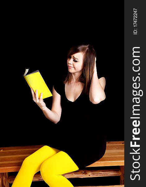 A woman wearing yellow tights in front of a black background scratching her head wiyh what is happening in the book. A woman wearing yellow tights in front of a black background scratching her head wiyh what is happening in the book.